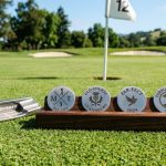 Set of custom engraved golf ball markers in stainless steel displayed on a golf green beside a putter