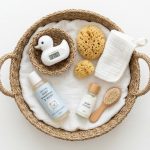 A flat-lay of baby bath items including a hooded towel and wooden brush on a marble background.