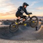 BMX rider jumping high over a concrete skatepark bowl at sunset.